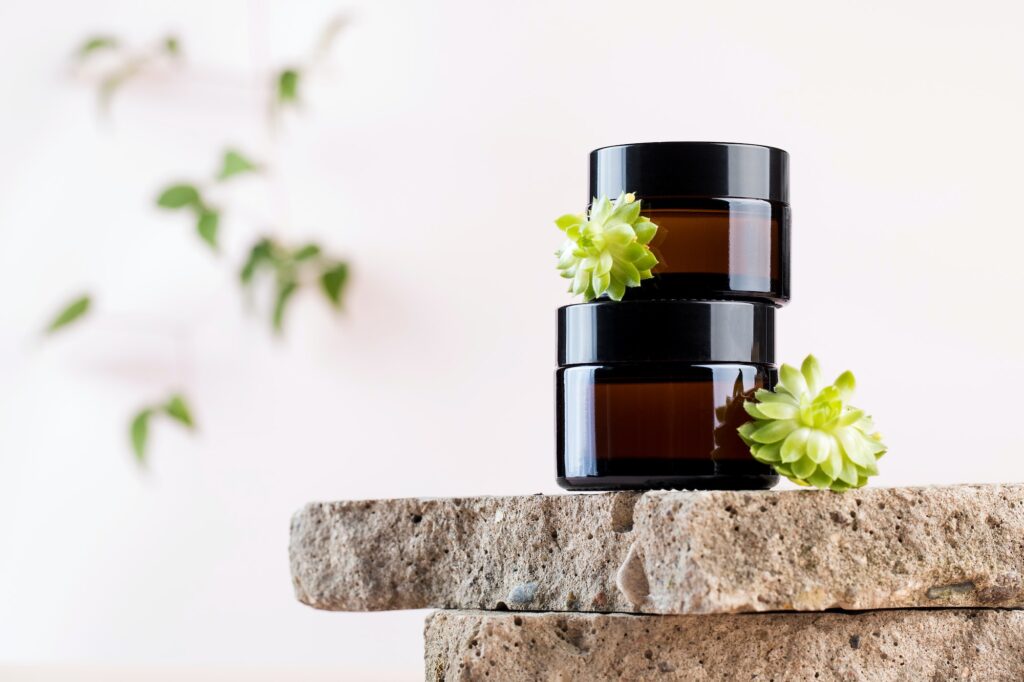 Jars with natural cosmetic products and succulents on concrete plates on pink