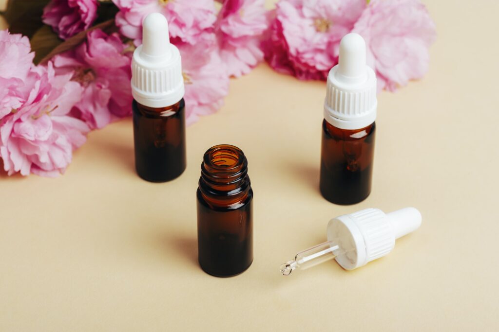 Brown glass bottles with essential oil and pink cherry blossom on beige background.