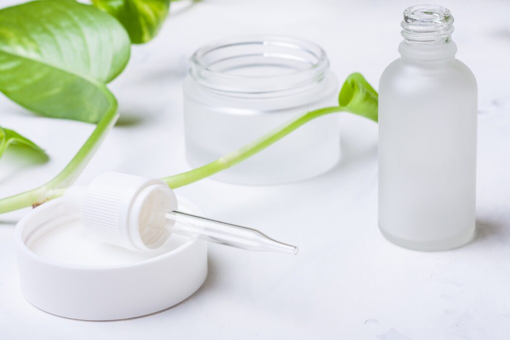 Glass bottles and jar for natural cosmetics on a white marble background