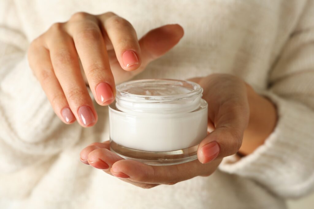 Woman in sweater with pink manicure hold jar of cosmetic cream