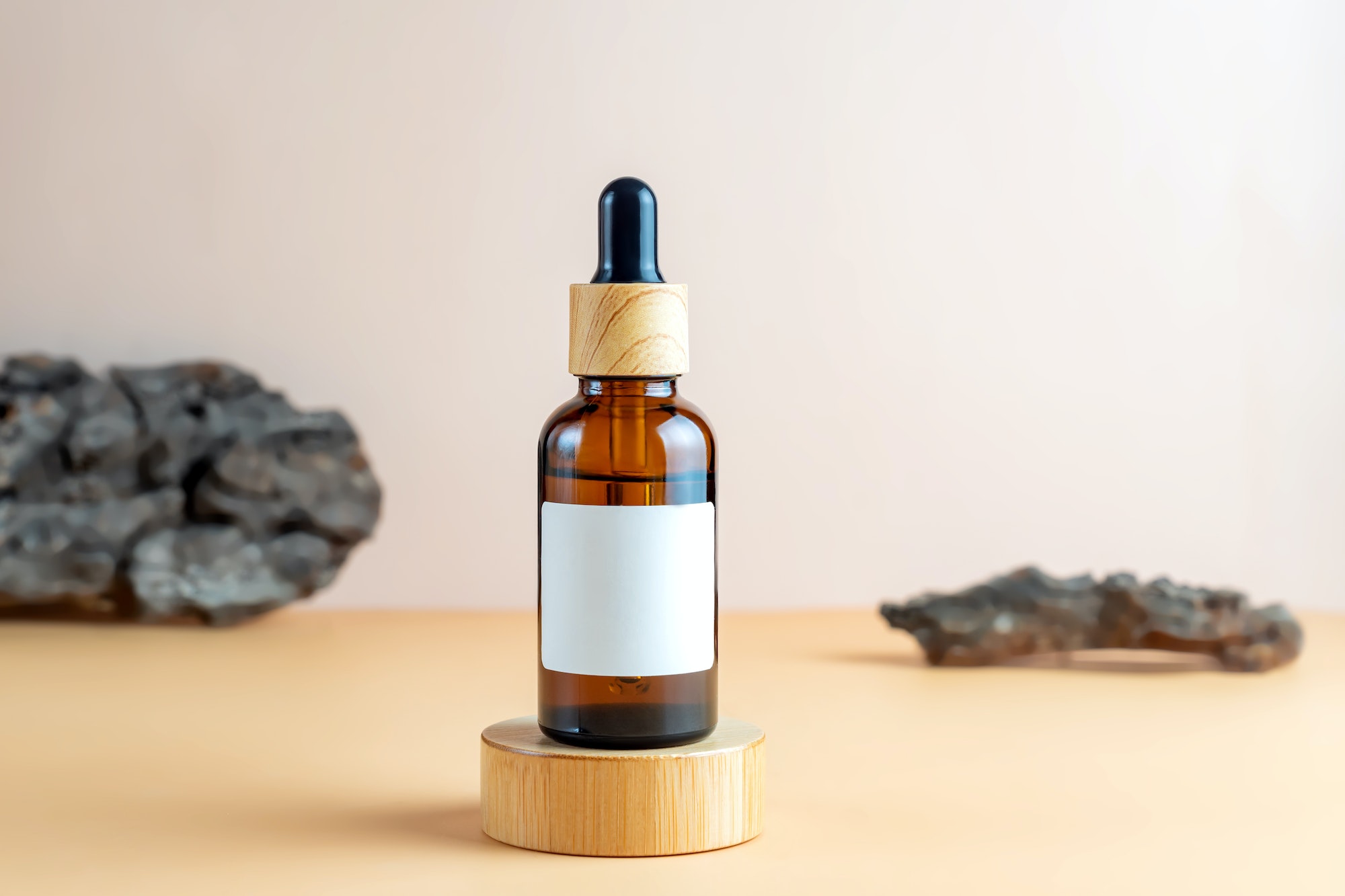 Amber glass cosmetic dropper bottle with blank label on round wooden podium.