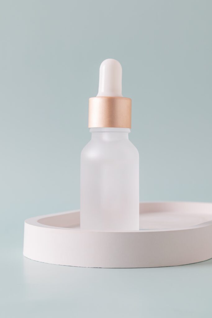 Frosted glass bottle with dropper pipette with serum or essential oil on concrete tray. Skincare