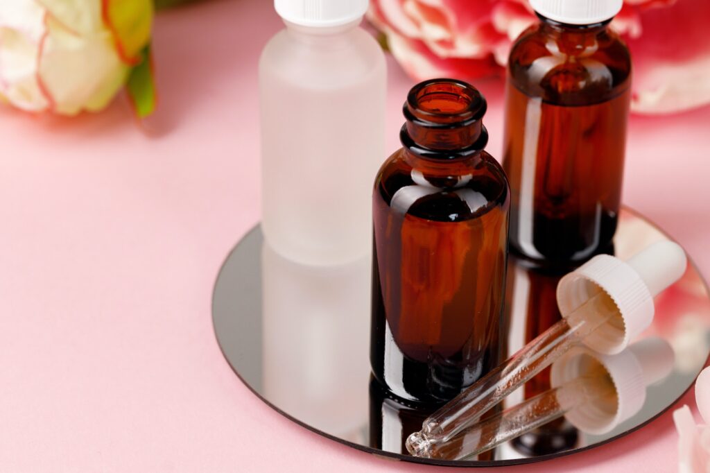 Glass bottle with oil on round mirror on pink background