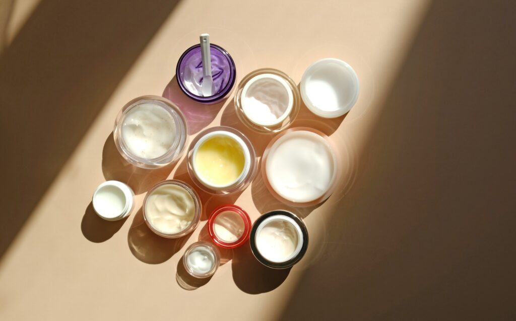 Many jars of beauty cream or mask for face care on pastel background, top view.