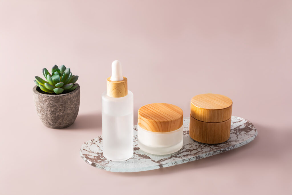 Natural cosmetics in frosted glass bottles and a jar with a bamboo lid on a tray. pastel background.