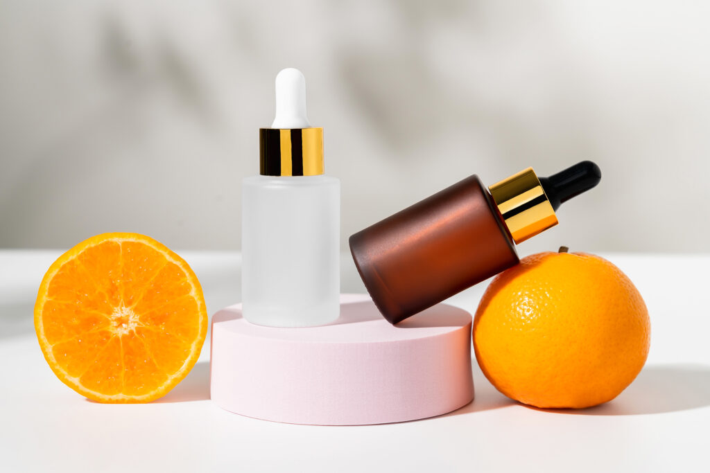 Serum bottle with dropper and slice of orange, ingredients for skin care on white background