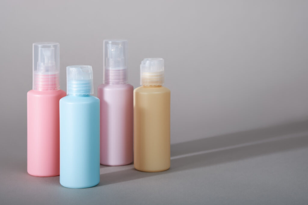 Travel kit. Set of four small plastic bottles for cosmetic products. Gray background with shadows.