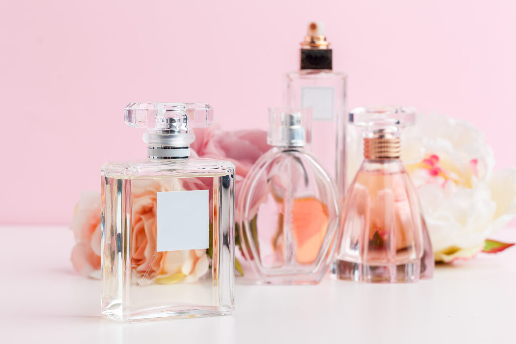 Bottle of perfume with flowers on color background