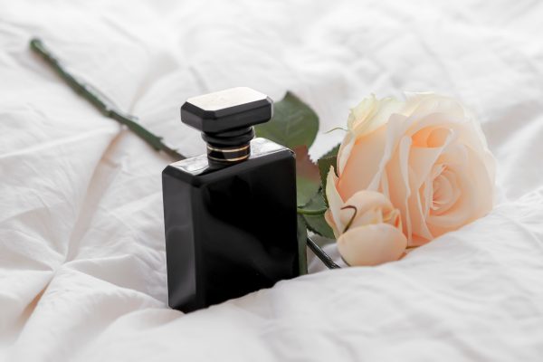 Closeup shot of black Perfume bottle on a white bed sheet with flower