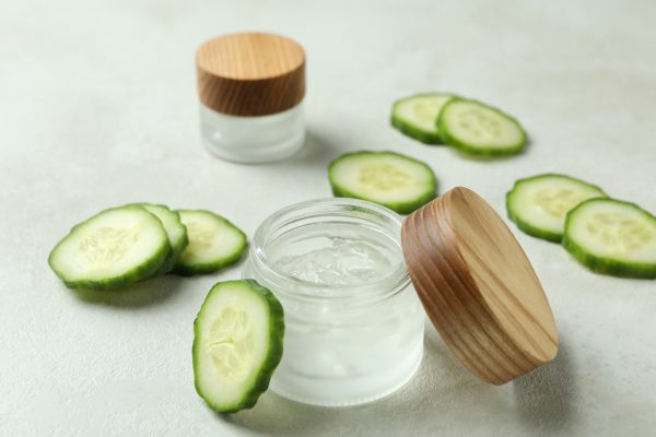 Jars with cosmetics and cucumber slices on white textured background